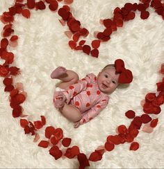 a baby laying in the shape of a heart surrounded by rose petals on a white rug