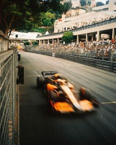 an orange race car driving down the street in front of a large group of people