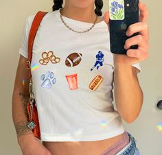 a woman taking a selfie with her cell phone while wearing a sports themed t - shirt