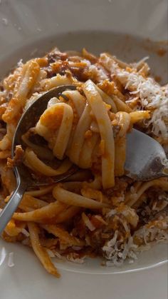 a white plate topped with pasta and meat covered in grated parmesan cheese