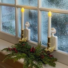 two candles sitting on top of a window sill next to a christmas wreath and pine cones