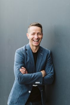 a smiling man leaning against a wall with his arms crossed