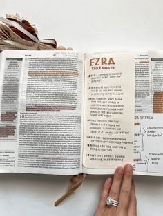 an open bible with the word ezra written on it and a person's hand pointing at it