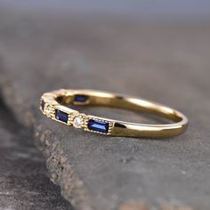 a yellow gold ring with blue sapphire stones on the inside and outside, sitting on top of a rock