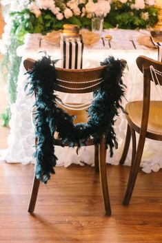 two chairs with black feathers on them are sitting in front of a white table cloth