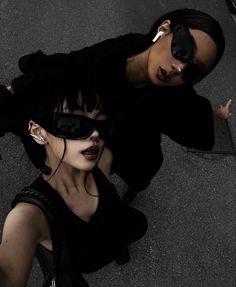 two people wearing sunglasses and black clothing standing next to each other on the ground with their arms around one another