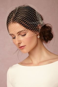 a woman wearing a birdcage veil with pearls on her head and hair comb