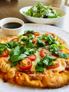 a white plate topped with a pizza covered in toppings next to a bowl of salad