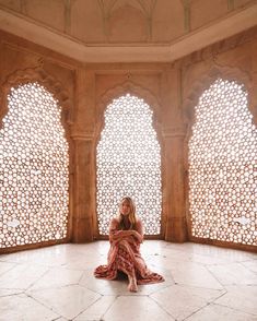 a woman sitting on the floor in front of two windows with intricate carved screens behind her