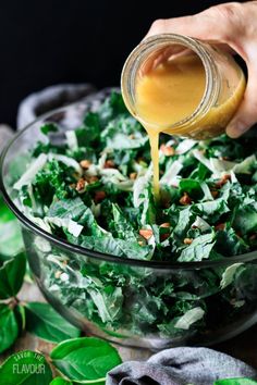 someone pouring dressing into a glass bowl filled with greens