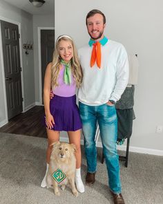 a man and woman standing next to a dog in front of a white wall with an orange ribbon on it