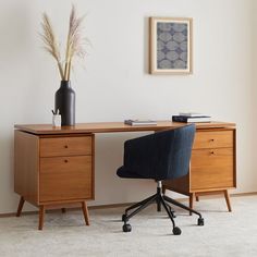 a wooden desk with a black chair next to it and a vase on the table