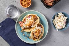 some food is sitting on a plate next to two bowls and one bowl filled with coleslaw