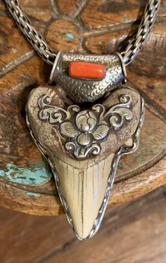 a necklace with an orange stone in the center on a wooden table next to a metal chain