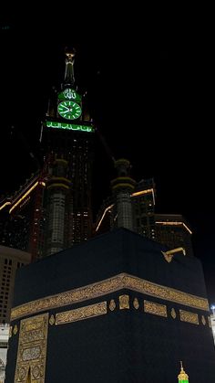 an illuminated clock tower in the middle of a city at night with skyscrapers behind it