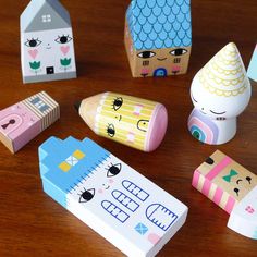 several small wooden toys on a table with paper houses and pencils next to them