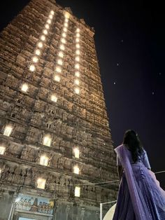 a woman standing in front of a tall building with lights on it's sides