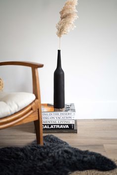 a black vase sitting on top of a stack of books next to a wooden chair