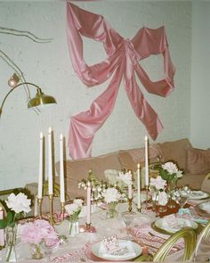 the table is set with pink napkins and white flowers, candles, and plates