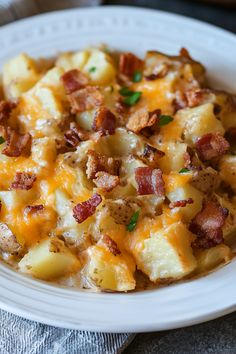 a white plate topped with potatoes covered in cheese and bacon next to a fork on a napkin