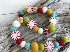 a christmas wreath made out of felt balls and candy canes on a piece of driftwood