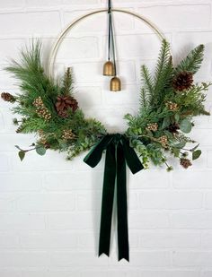 a wreath with pine cones, evergreens and bells hanging on a wall in front of a white brick wall