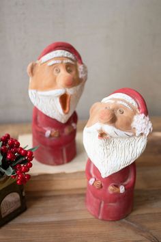 two santa claus figurines on a wooden table next to a potted plant