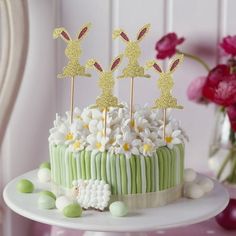 a green cake with white flowers and gold bunny toppers on it sitting on a table