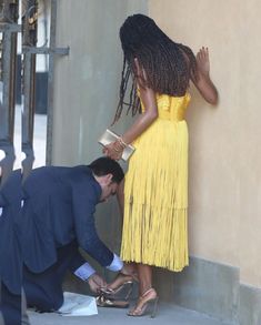 a woman in a yellow dress leaning against a wall