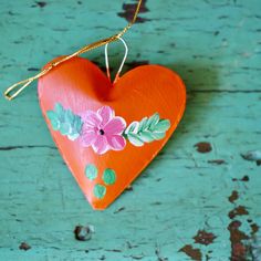 a heart shaped ornament hanging from a string on a green wooden surface with leaves and flowers painted on it