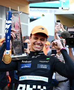 a man holding up a trophy in front of a group of people with cameras around him