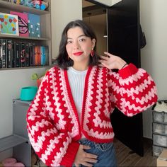 a woman wearing a red and white knitted cardigan standing in front of a bookshelf