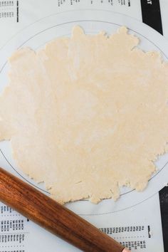 a person holding a rolling pin on top of a pizza dough with an uncooked pizza crust next to it