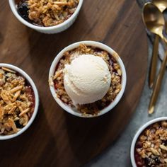 four bowls filled with granola and ice cream on top of a wooden table next to spoons