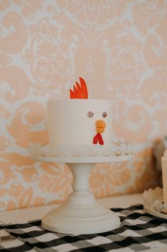 a white cake with a red rooster on top sitting on a black and white checkered tablecloth