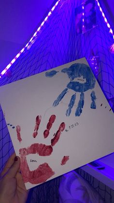 a person holding up a piece of paper with handprints on it in front of a purple light