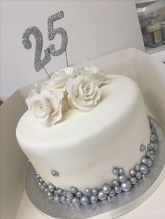 a white cake with flowers and pearls on the bottom is decorated with a number twenty five