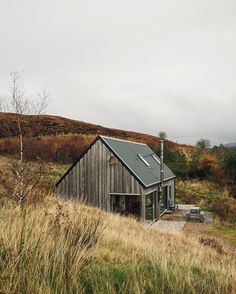 a small wooden house sitting on top of a grass covered hill next to a forest