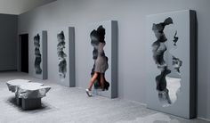 a woman is walking through an art gallery with sculptures on the walls and tables in front of her