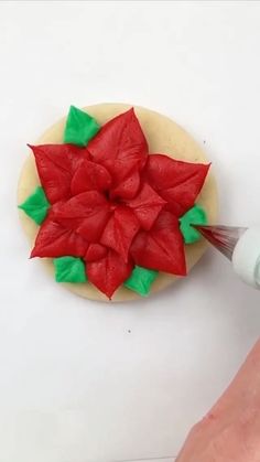 someone is decorating a poinsettia cookie with icing and green leaves