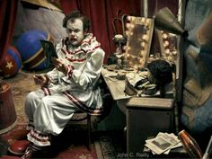 a creepy clown is sitting in front of a vanity mirror and looking at his cell phone