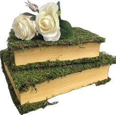 three books covered in moss and flowers on top of each other with white roses sitting atop them