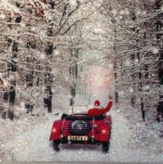 a car driving down a snow covered road with santa clause on the roof and arms in the air