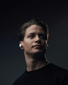 a man with ear rings on his ears looking off to the side, against a dark background