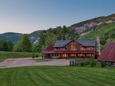 a large house in the middle of a lush green field with mountains in the background