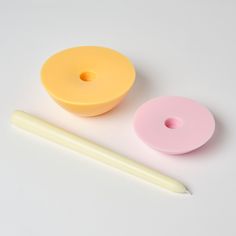 two yellow donuts and a pink donut on a white surface next to a pencil