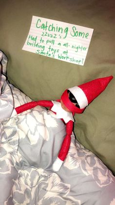 an elf laying in bed with a sign on the pillow