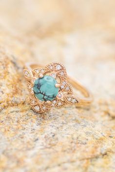 a gold ring with a turquoise stone surrounded by white and clear diamonds on a rock