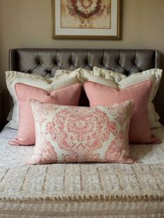 a bed with pink and white pillows on top of it next to a framed painting