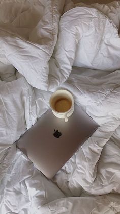 an apple laptop computer sitting on top of a bed covered in white sheets and pillows